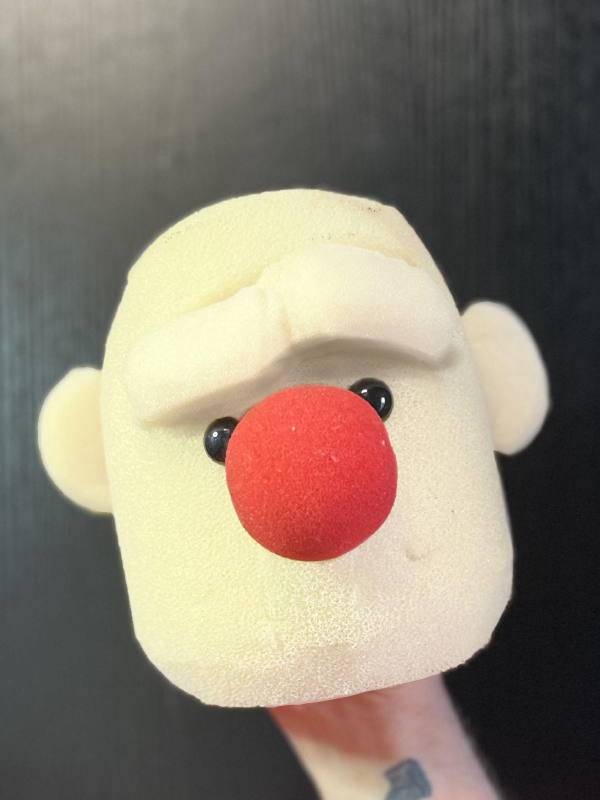 Close-up of a foam clown-face puppet head with a red nose and big round ears