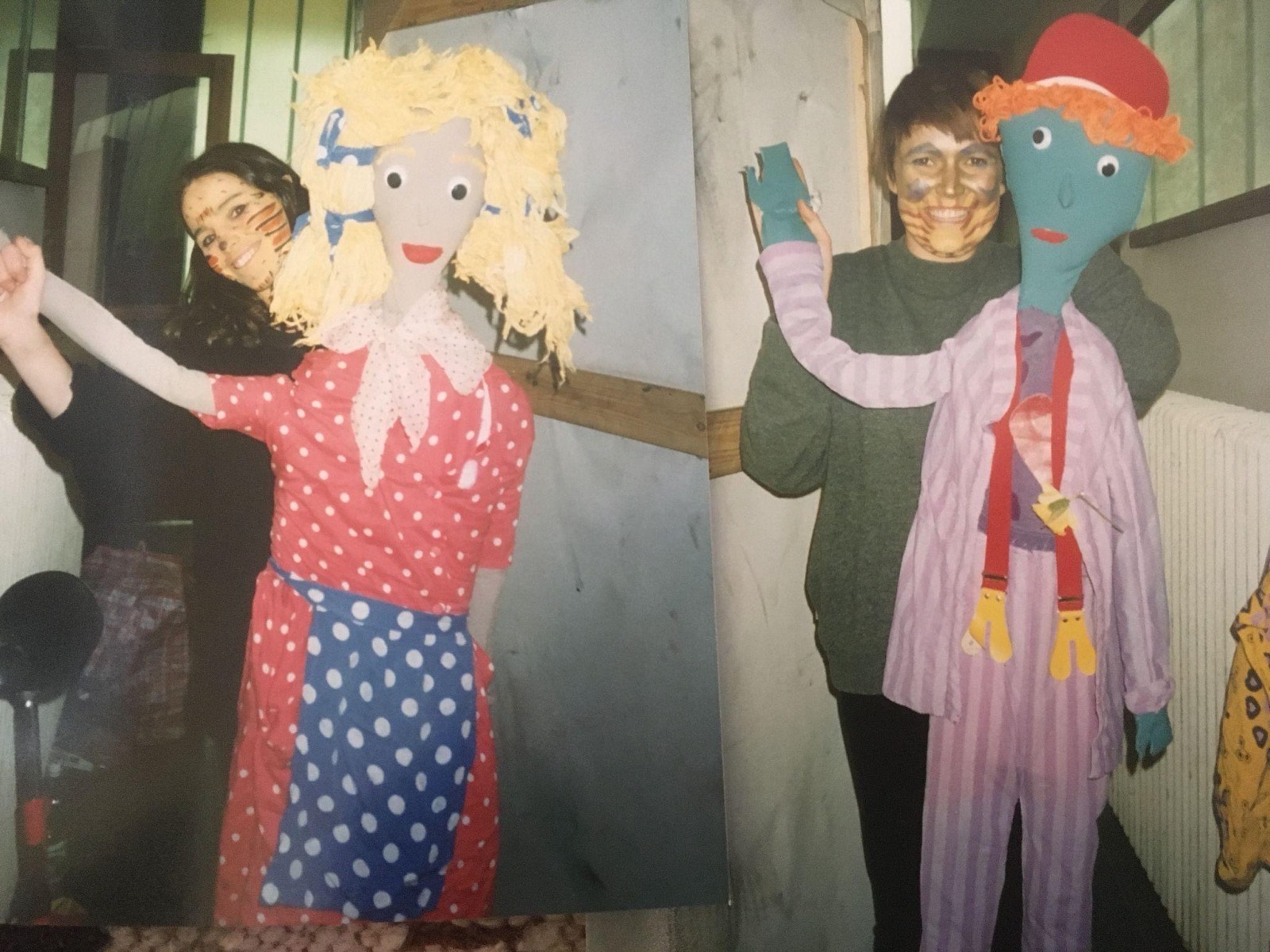 An old photograph of two performers posing beside large costumed puppet figures, one in a polka-dot dress, one blue-faced in striped pyjamas