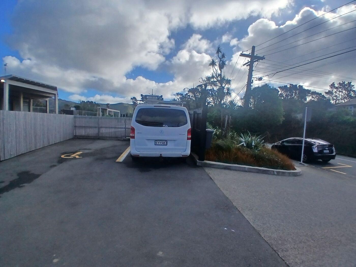 Two car parks marked with a wheelchair symbol on the sealed driveway in front of Ridgway School, with a van parked in one space. A wooden paling fence runs along the left side of the driveway.
