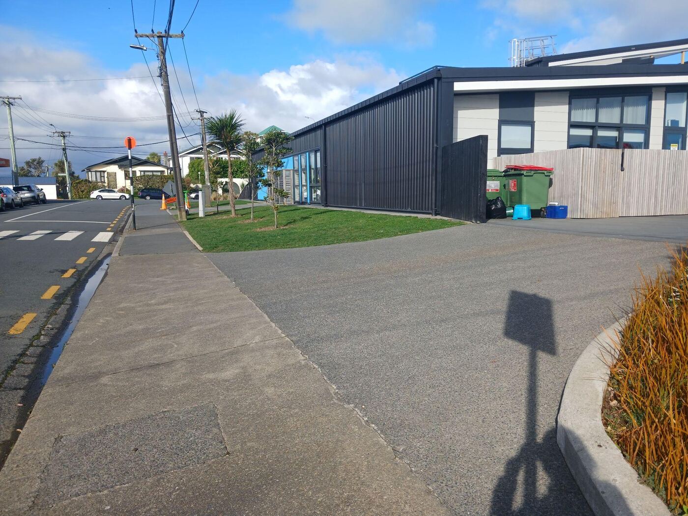 The footpath along Mornington Road where it crosses the entrance to the Ridgway School driveway. The path is flat sealed concrete at street level, with the dark-clad school building and a wooden fence on the right and houses further down the street.