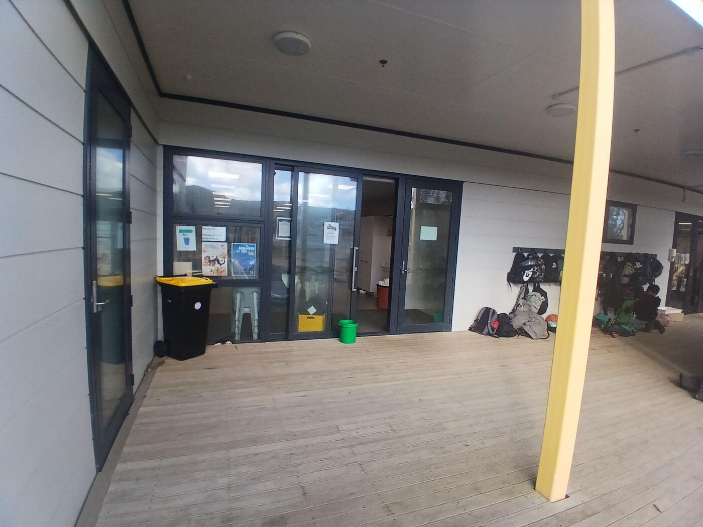The covered wooden deck leading to a set of dark-framed glass double doors, one of them propped open. Bike racks stand to one side, and the deck is level all the way to the doors.